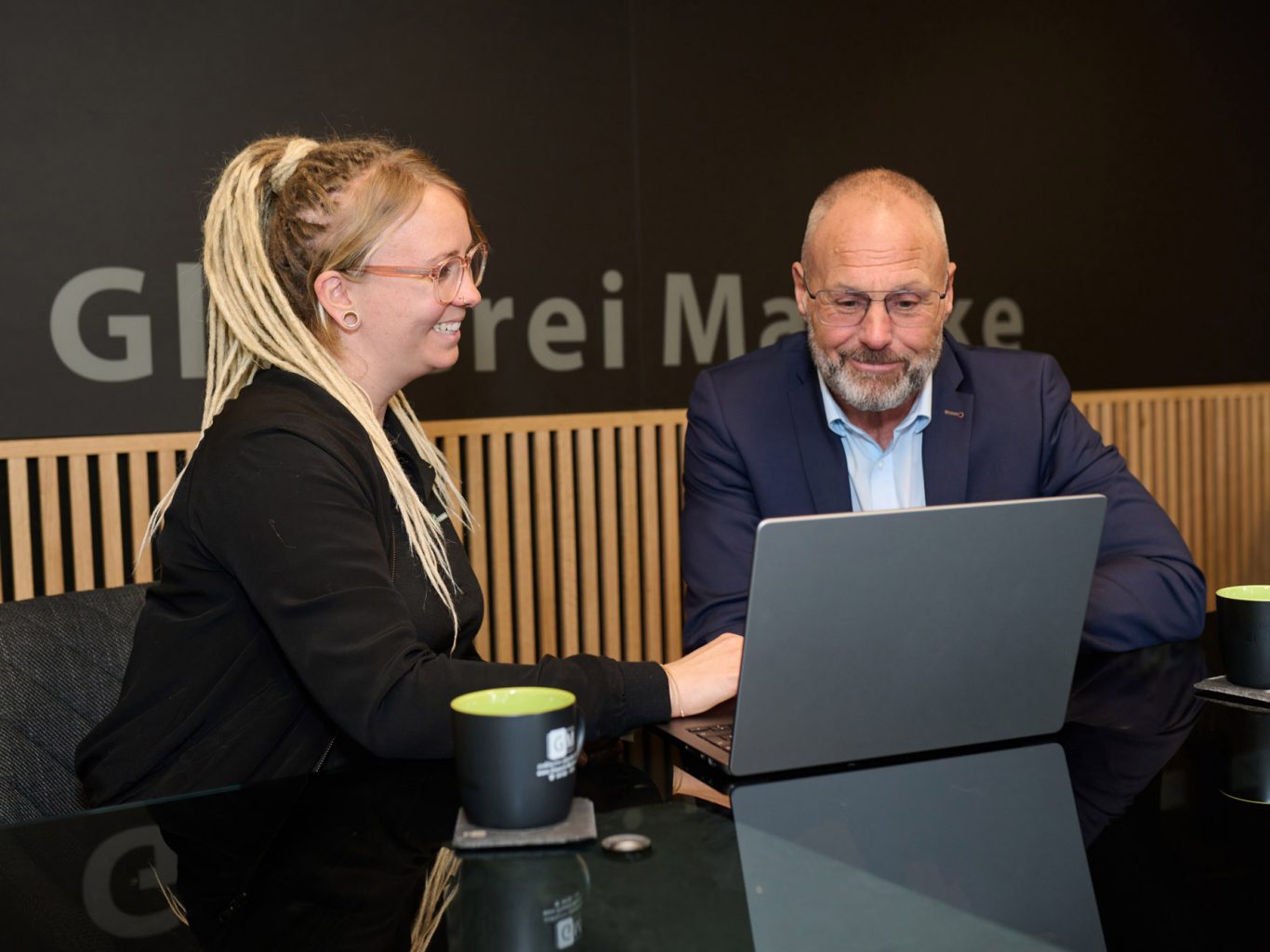 Kim Burmeister zeigt dem Firmenkundenberater Matthias Hermann am neuen Laptop den Social Media-Auftritt der Glaserei.