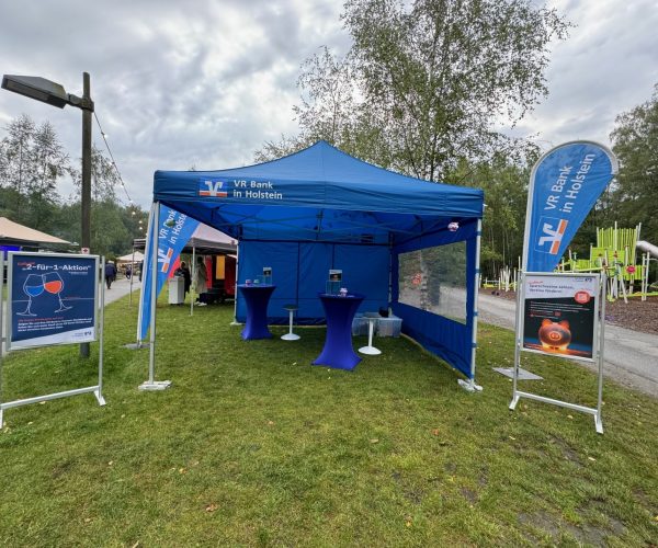 Ein Blauer Pavillon mit blau-orangener Beschriftung auf einer herbstlichen Festwiese